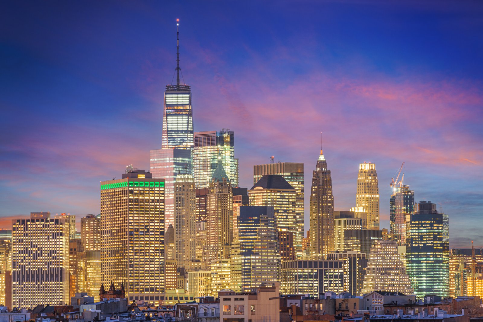 Lower Manhattan cityscape with iconic skyscrapers, historic buildings, and the New York Harbor in the background